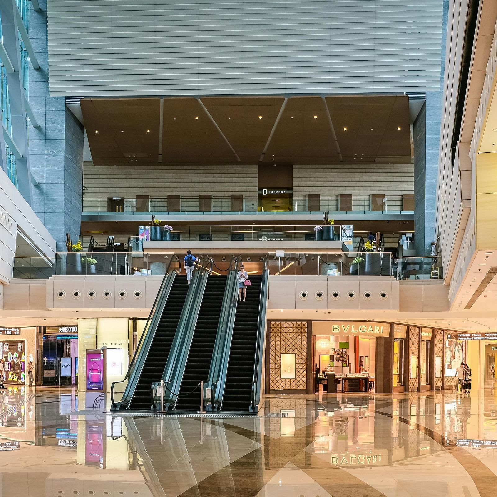 A bustling mall featuring escalators and shoppers navigating various stores.